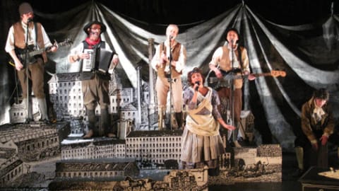 Musicians in Victorian peasant clothing stood in a model of industrial England