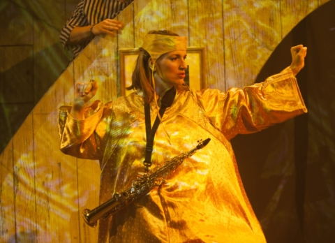 A woman with a large yellow dress and a musical instrument around her neck, dancing