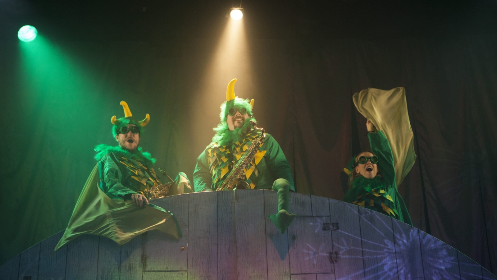 Three Actors with green and yellow costumes, with feathers, horns and wings.