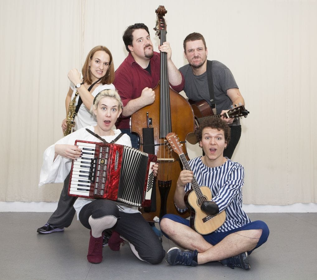 Five actors posing with various musical instruments