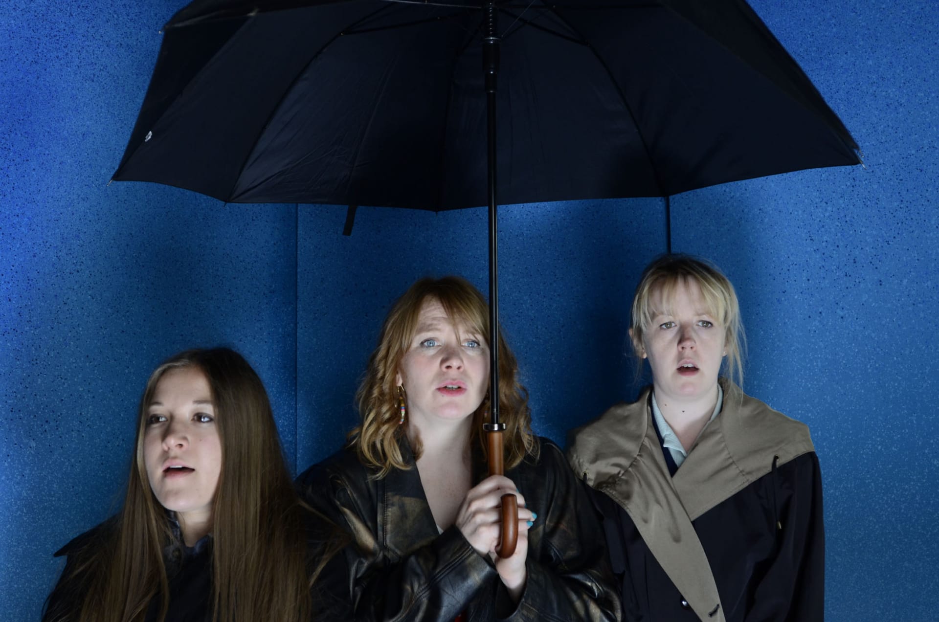 Three women stood under an umbrella