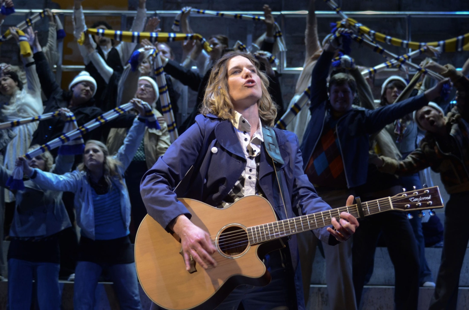 A woman playing guitar with a crowd of football fans behind her