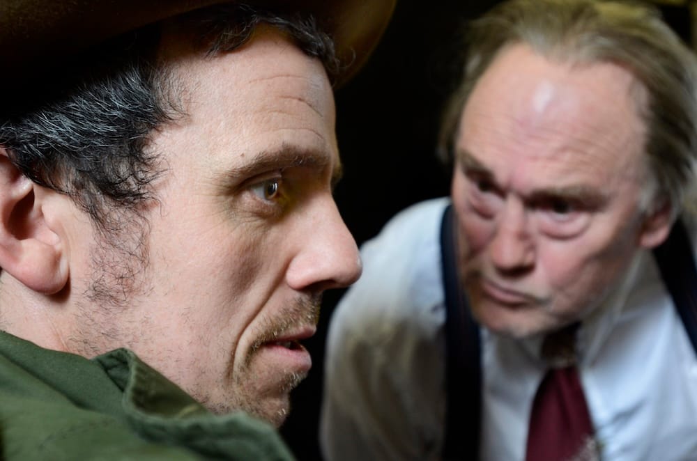 An older man in a suit glaring with his face close to another man in a parka coat