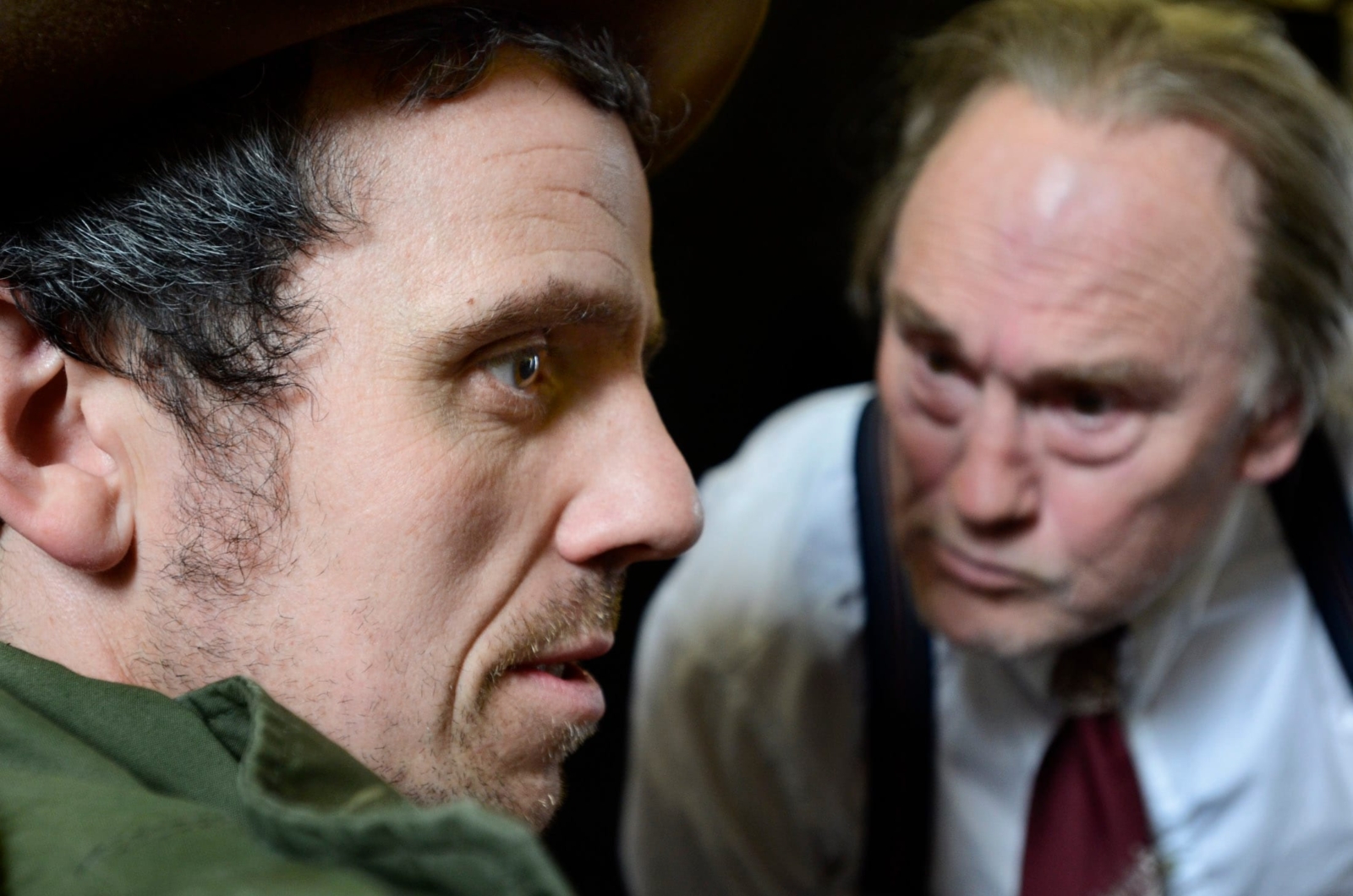 An older man in a suit leaning menacingly close to a younger man in a parka