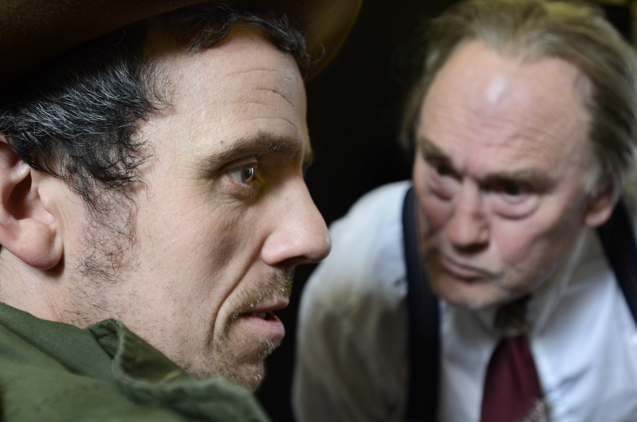 An older man in a suit leaning menacingly close to a younger man in a parka