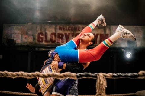 A wrestler holding another upside down and straining in a gym