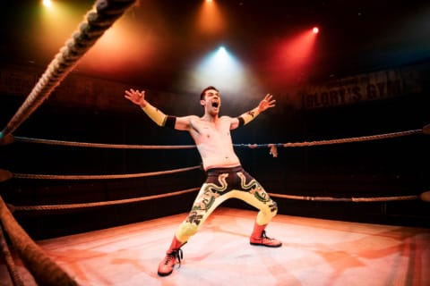 A wrestler with arms and legs spread widely whilst shouting in a gym