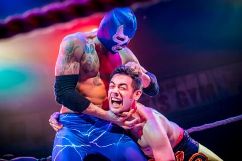 A wrestler in a mask holding another wrestler by the hair