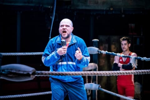 A wrestling coach shouting into the microphone hanging from the ceiling