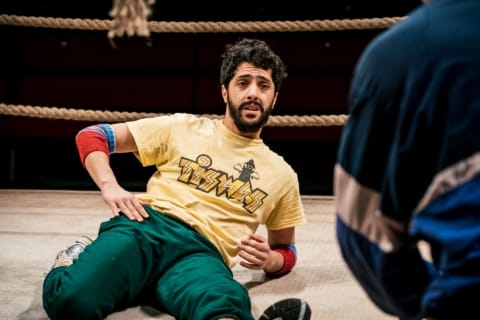 A wrestler casually laying on the ring floor, listening to his coach