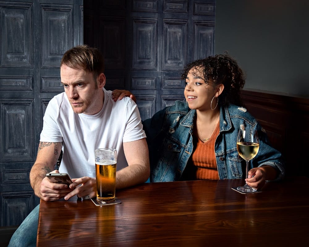 A man and a woman at a pub, both with drinks. The wioman is talking to the disengaged man.