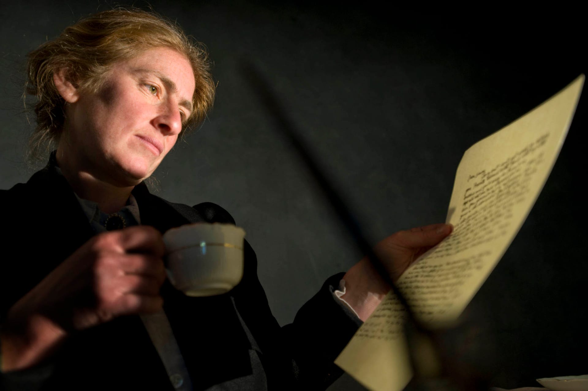 Woman looking at a letter, with a hot drink in hand.