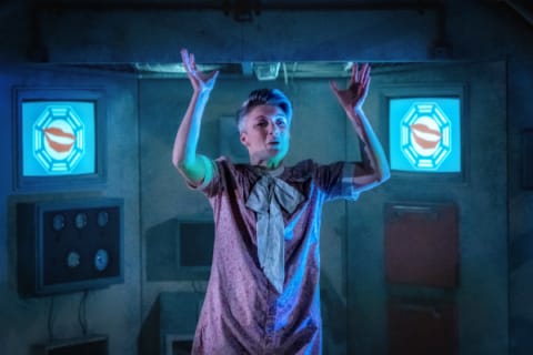 A woman in a dystopian chamber with arms raised