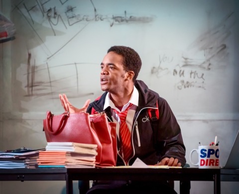 A teenage pupil sat at his desk pointing his finger whilst telling a story