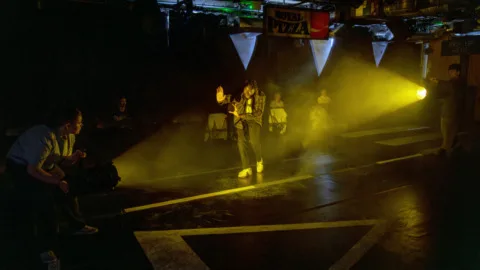 A taxi driver walking towards a bright light with his arms in front of him