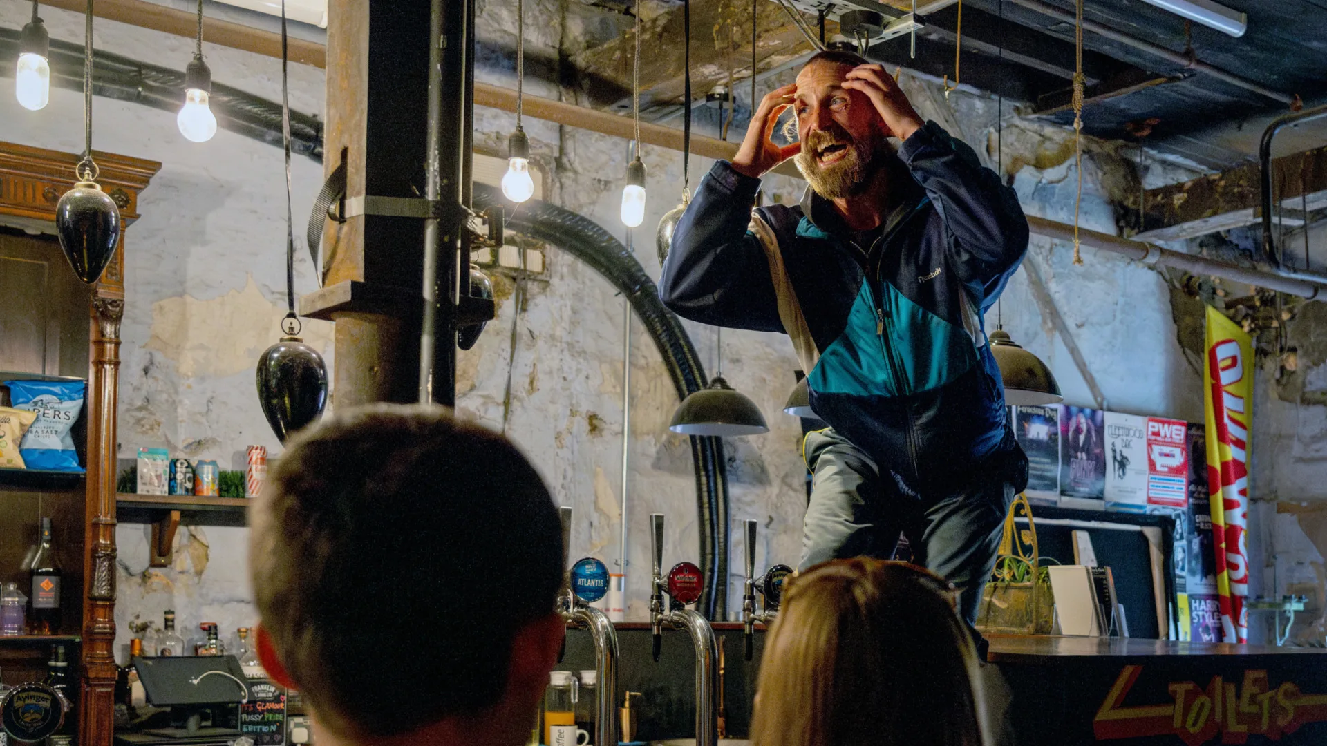A man stood on a bar manically gesturing to his head