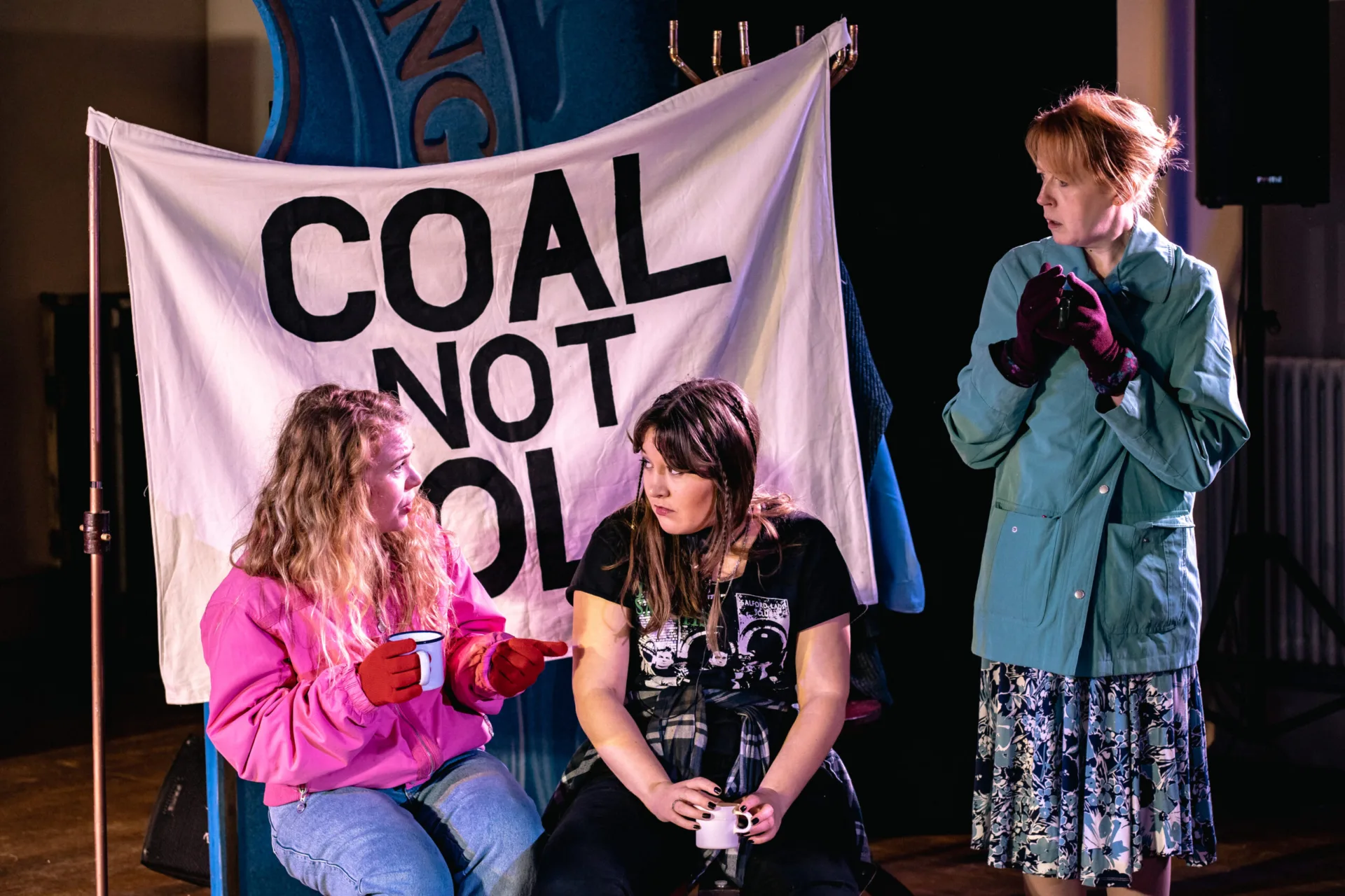 Three women with a sheet with Coal Not Dole painted on in winter clothes and tin mugs