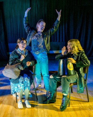 Three sisters singing and dancing using a collection bucket for a drum