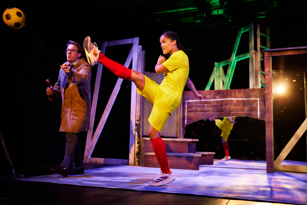 A girl in football kit kicking a ball on stage