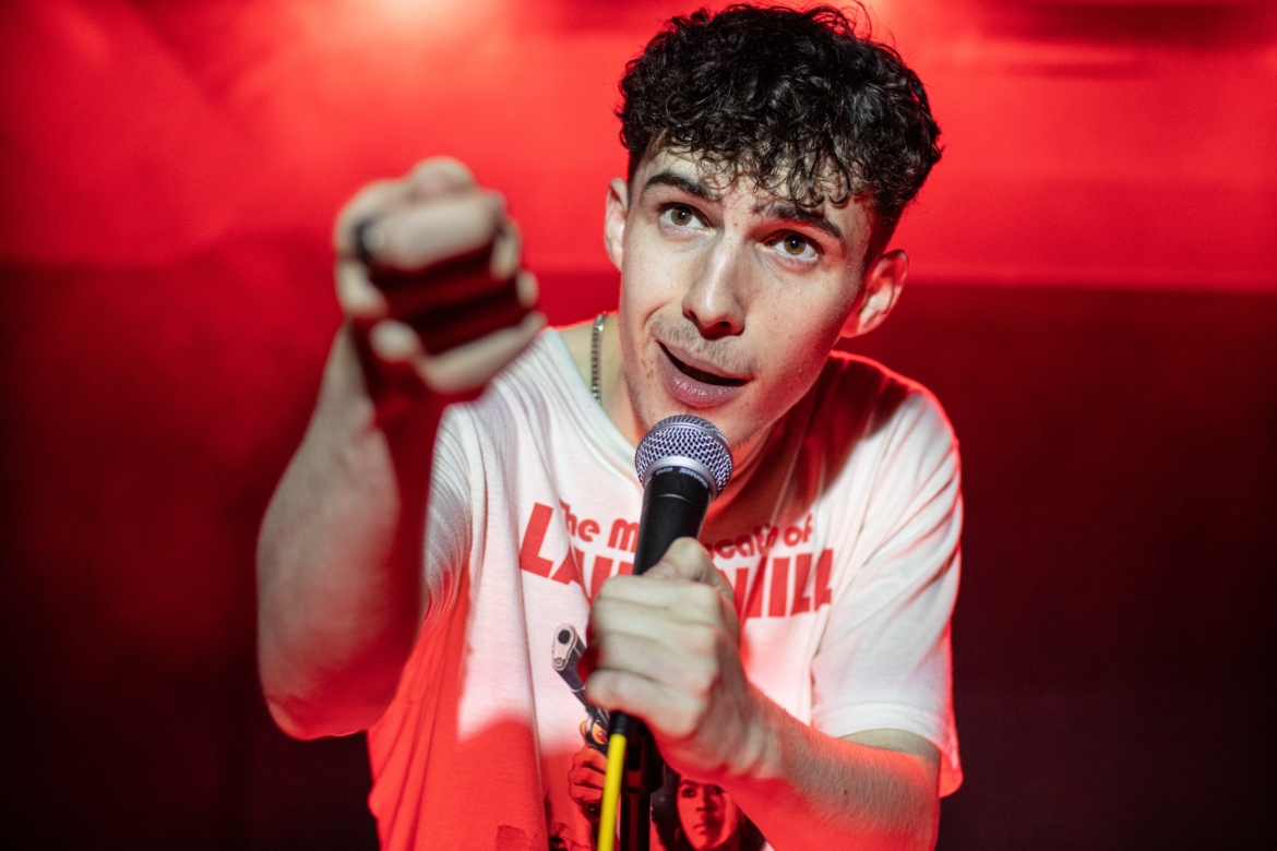 A young man with a microphone pointing aggressively as if into your face