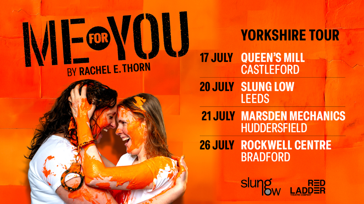 Two women holding each other and laughing, covered in orange paint