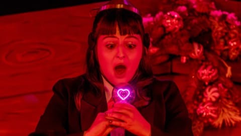 A woman dressed as a robot staring at a glowing heart in a lightbulb