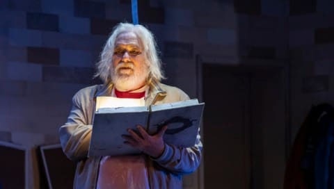 A man with long grey hair reading a large book