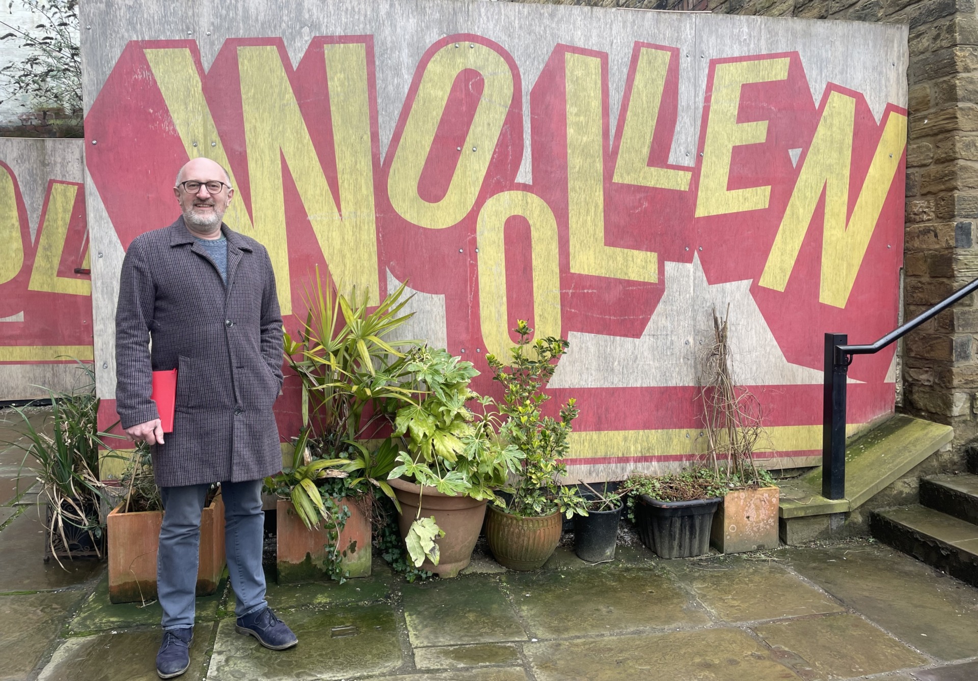 Dick stood smiling in front of a wooden mural for his venue Old Woollen
