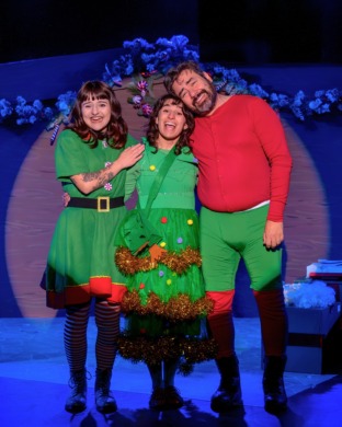 A half-dressed Santa, elf and someone dressed as a christmas tree singing and hugging