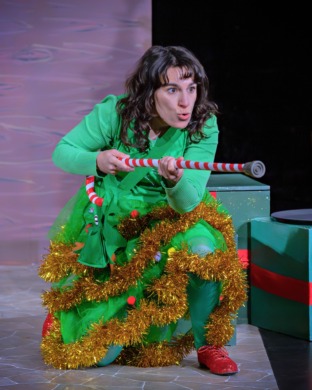 A woman dressed as a Christmas tree holding a candy cane like a gun