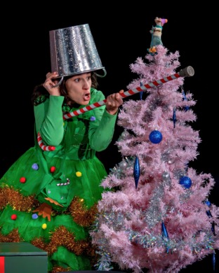 A woman dressed as a christmas tree hiding and using a bucket as a helmet and cane as a gun