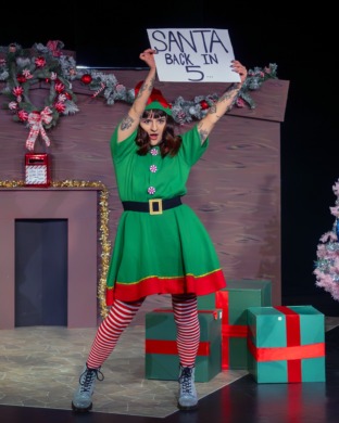 A woman dressed as a christmas elf holding a sign up like a hostess at the boxing.