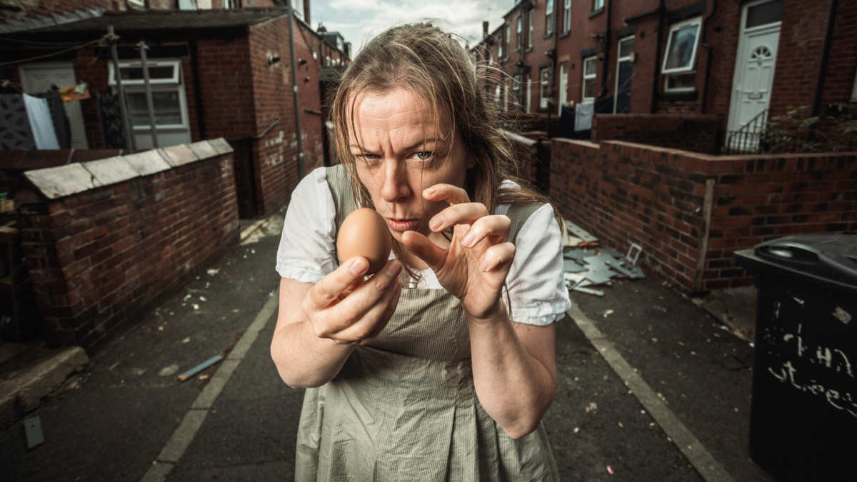 A woman in early 19th century peasant clothing menacingly holding an egg