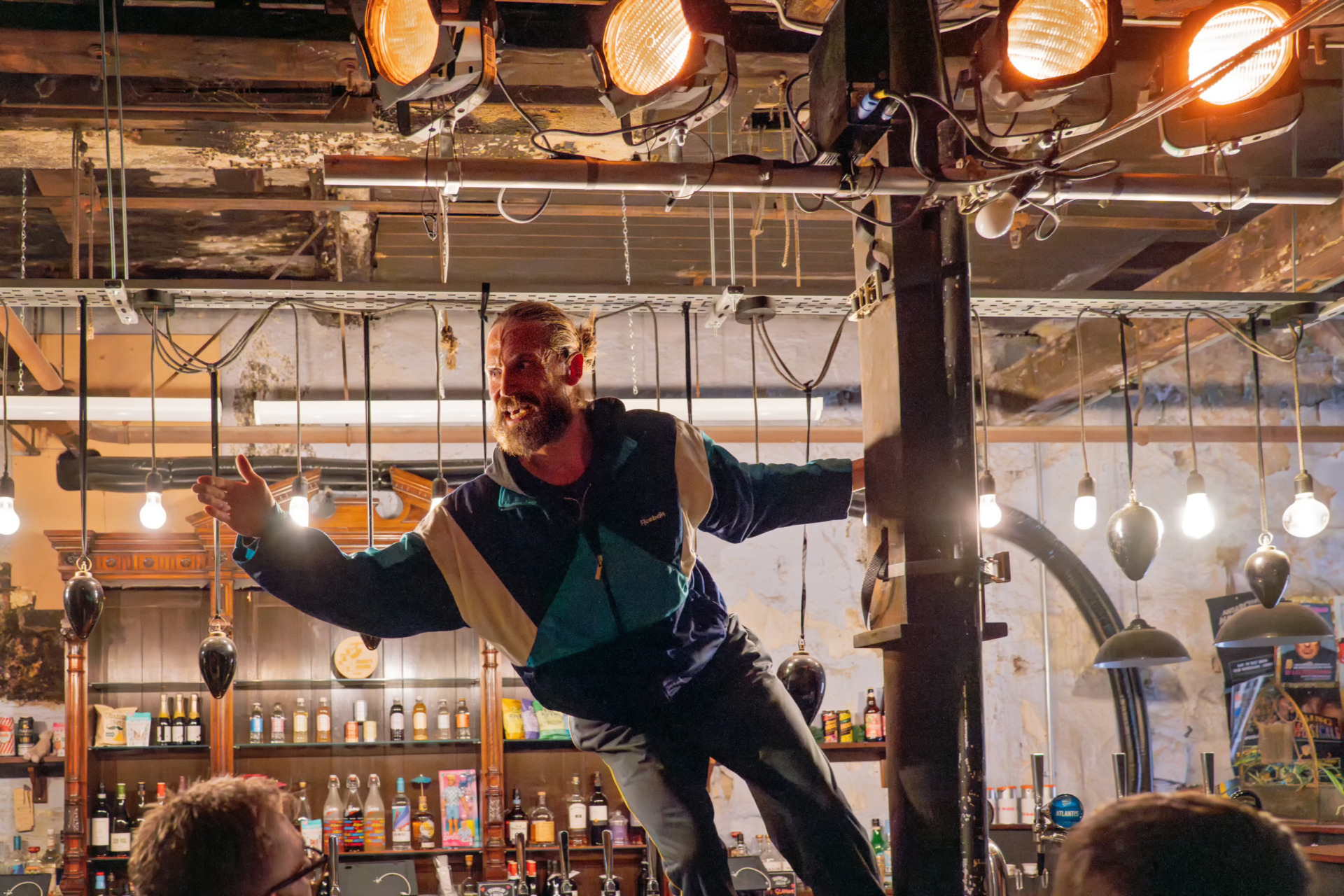 A man swinging from a column whilst stood on a bar addressing an audience
