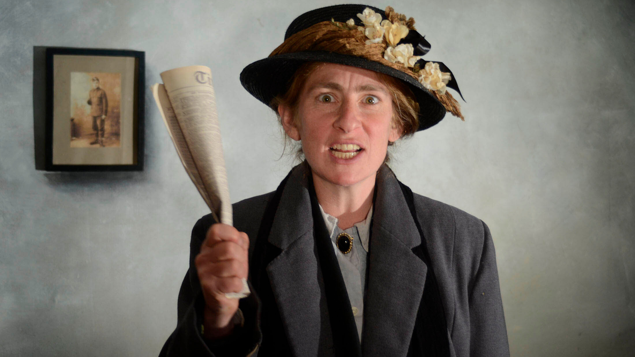 A woman in early 20th century dress holding a newspaper in her fist