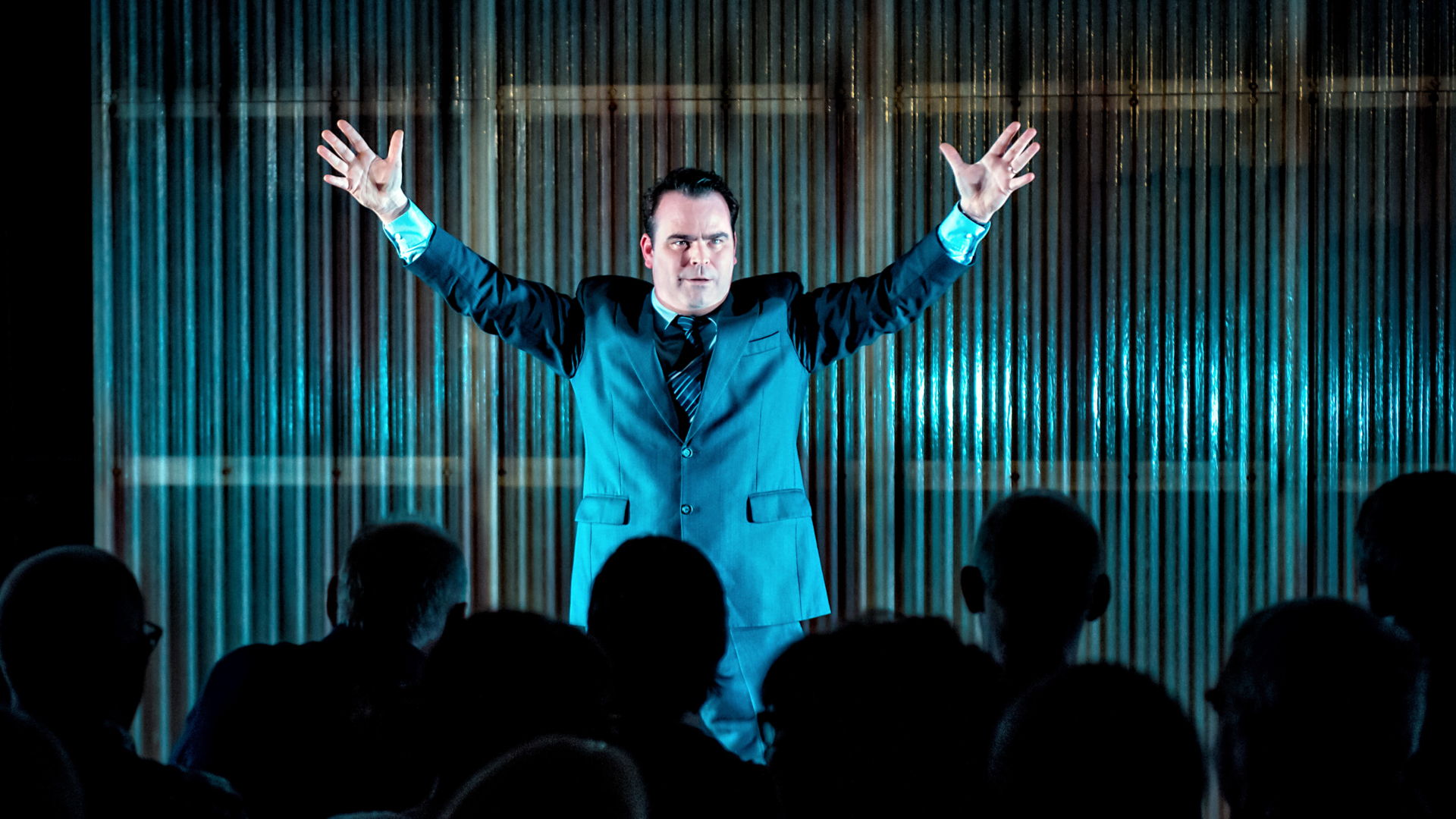 A man in a suit with arms outstretched addressing an audience