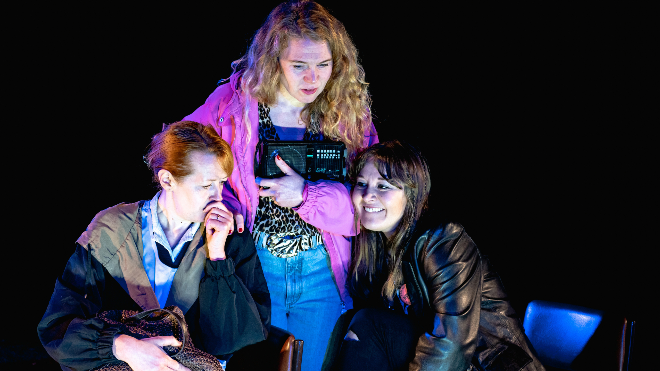 Three women gathered round a radio listening intently