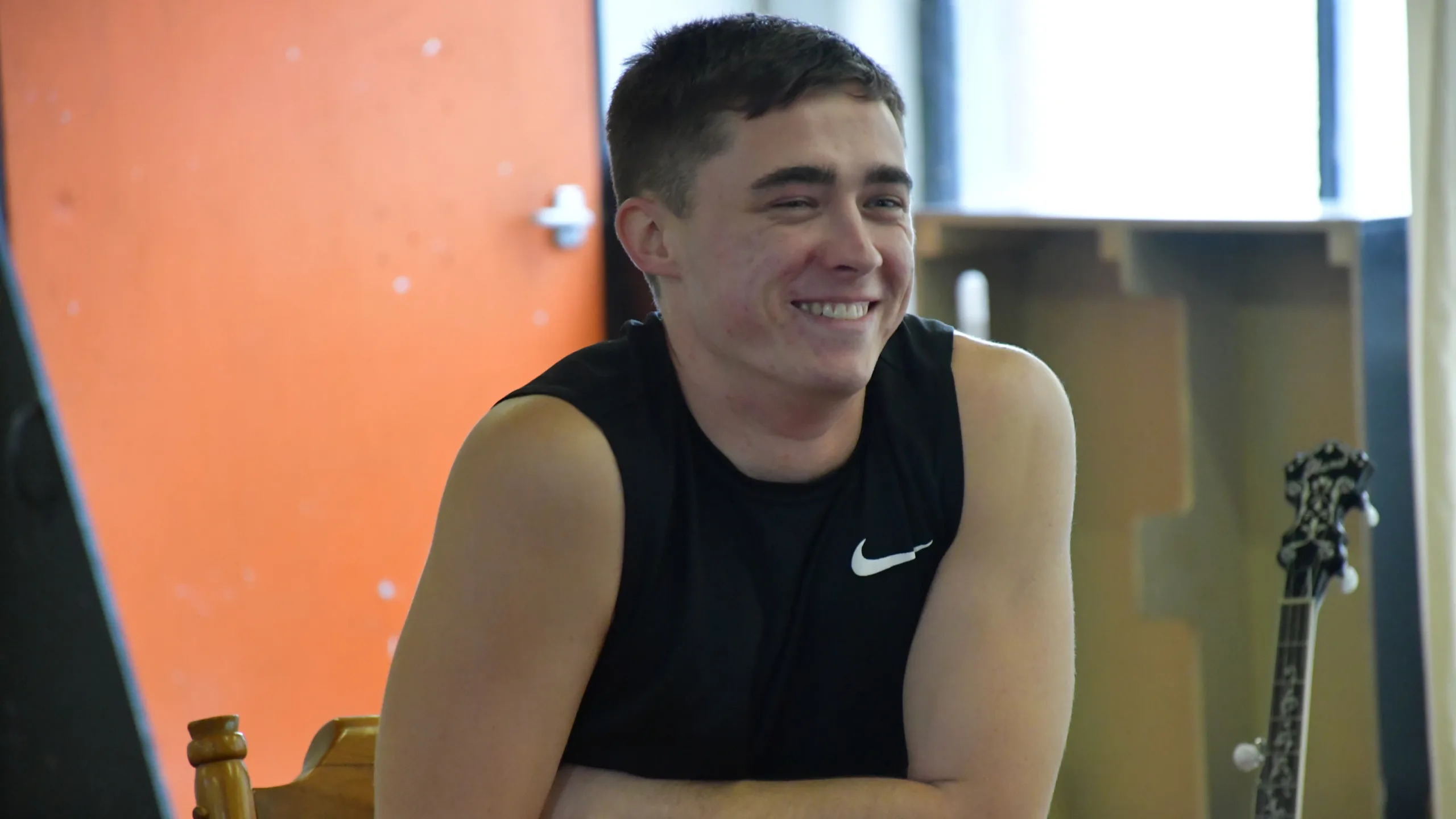 Tyler in vest leaning on desk in rehearsal room and smiling