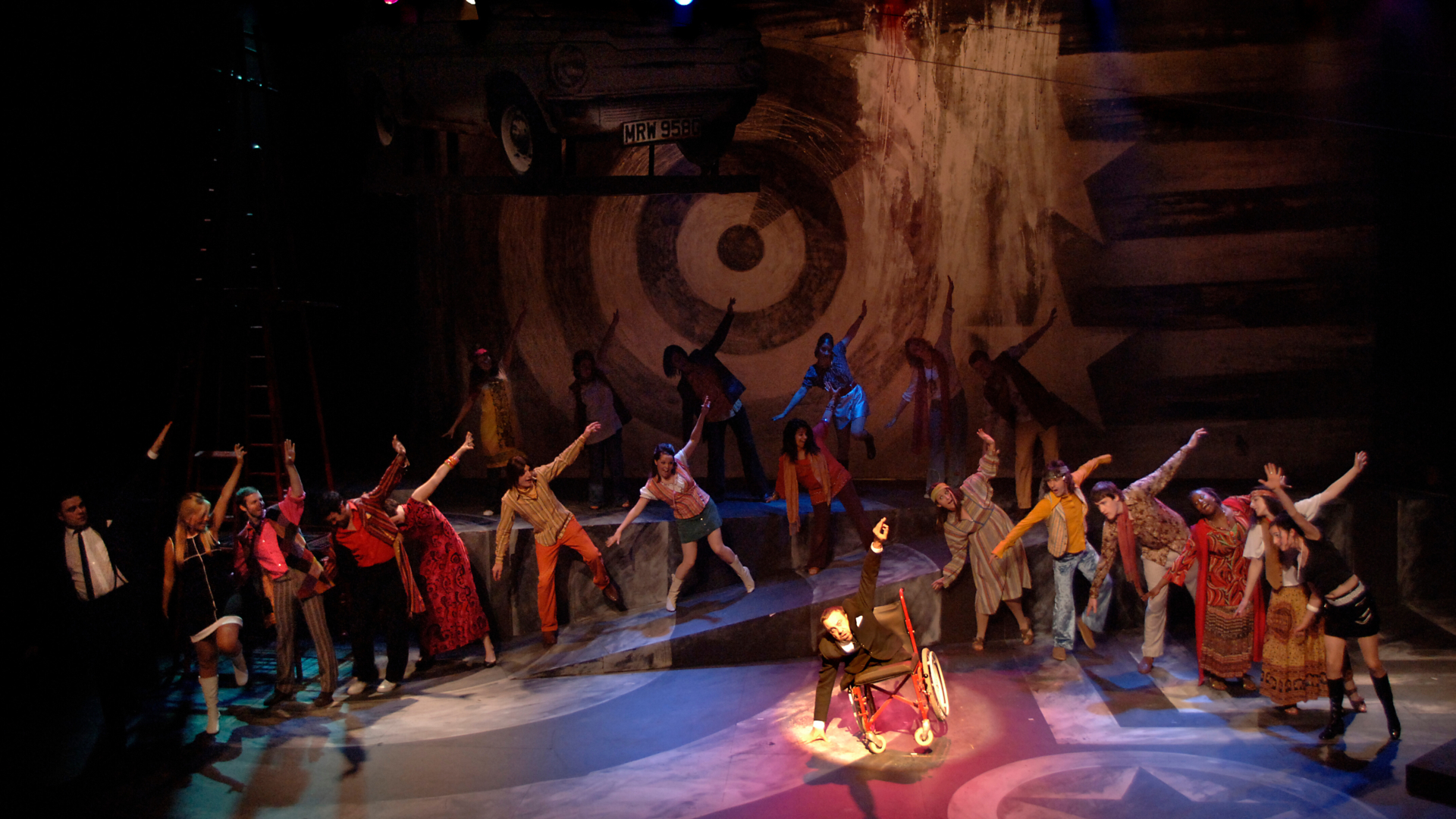 A chorus dressed in 60s and 70s costumes dancing onstage