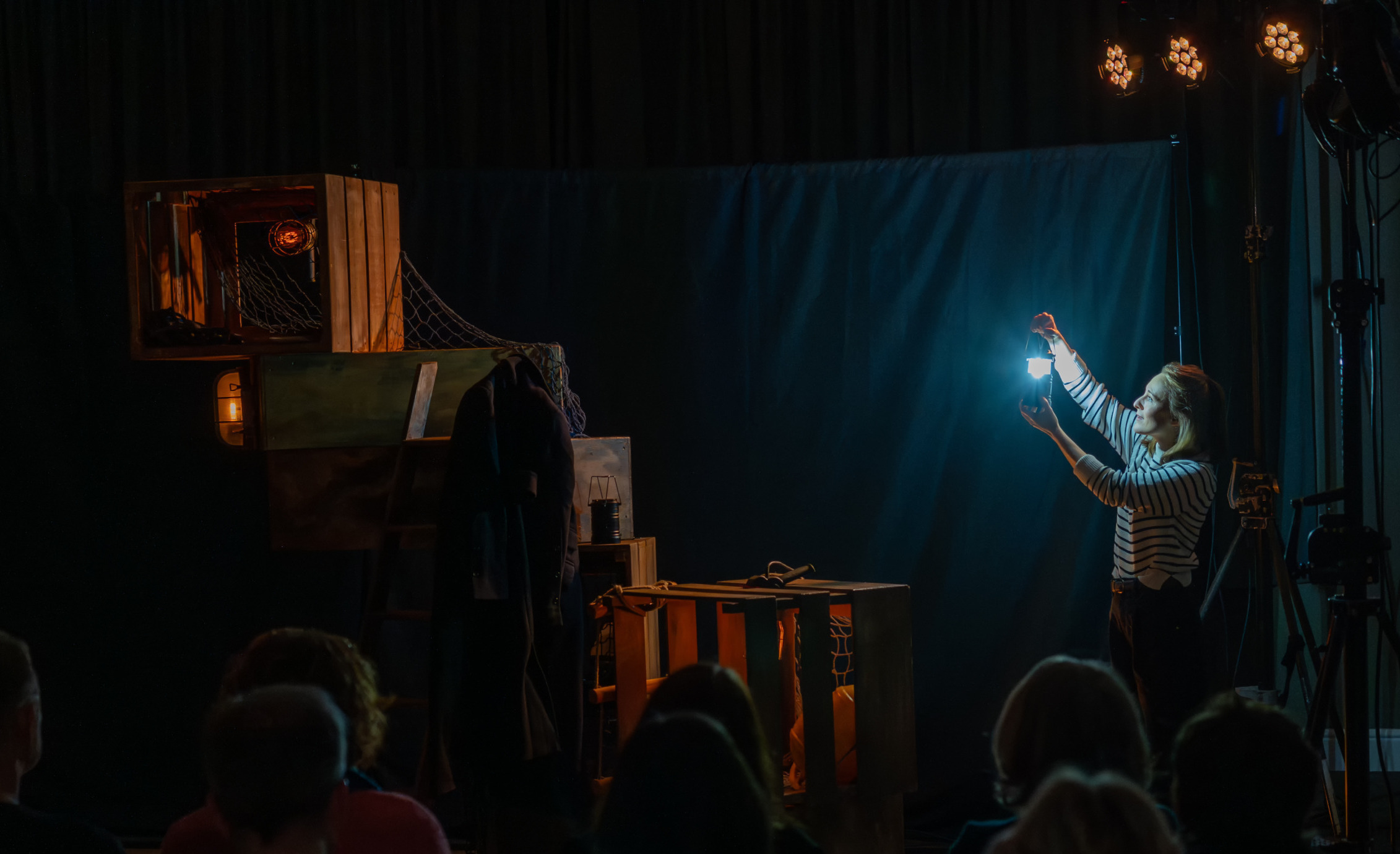 A woman holding up a lantern on a dark stage in front of an audience