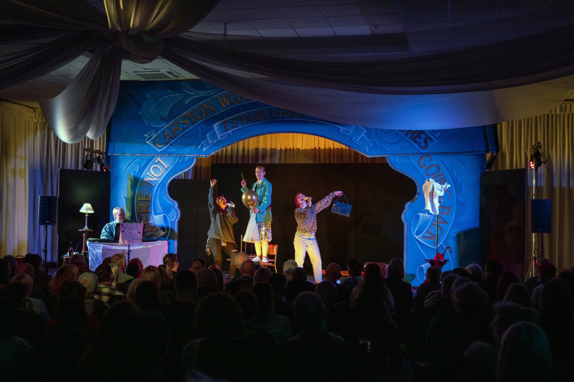 Four women singing and dancing on stage in a large event space