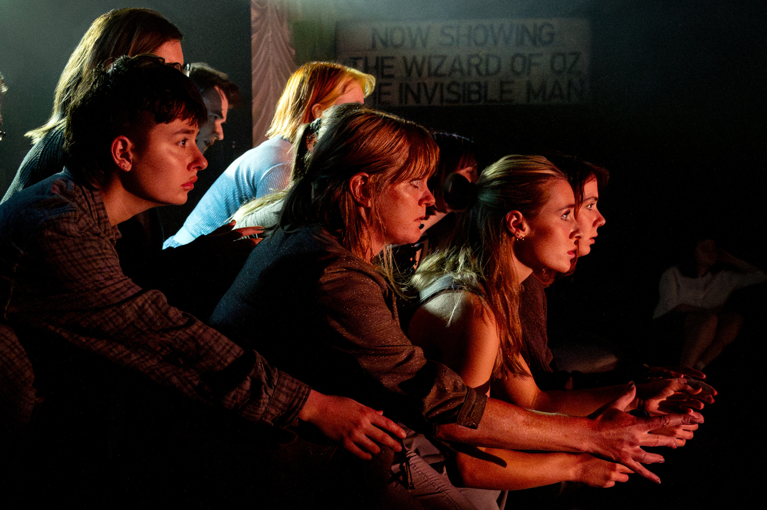 A group of people leaning forward with eyes fixed forward under theatre lights