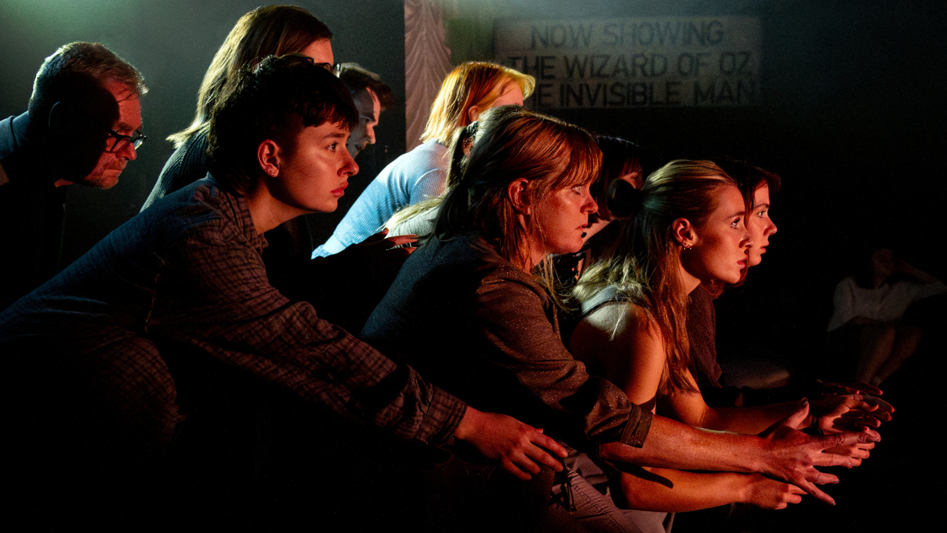 A group of people leaning forward with eyes fixed forward under theatre lights