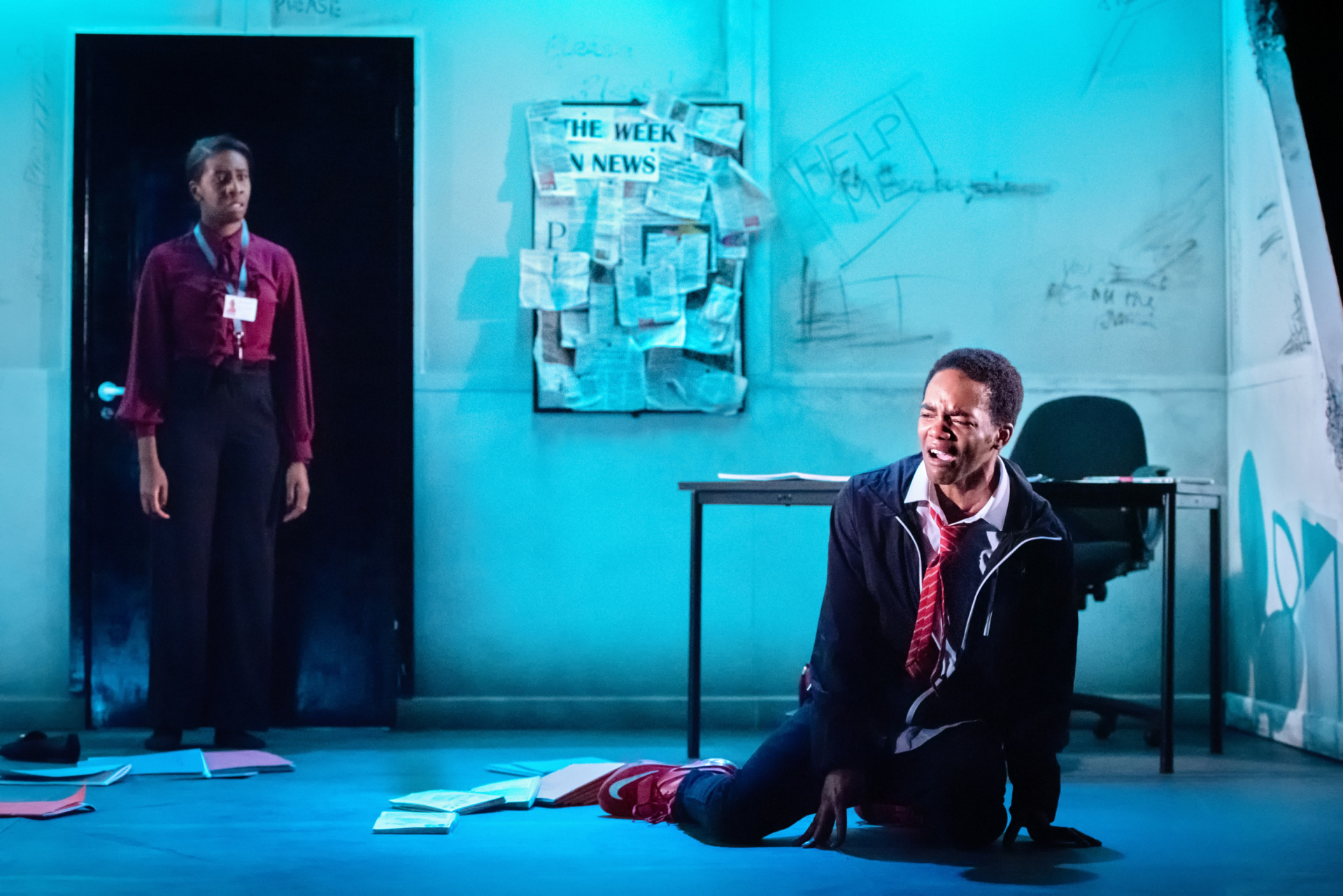 A teenage boy on the floor crying as his teacher watched from a doorway