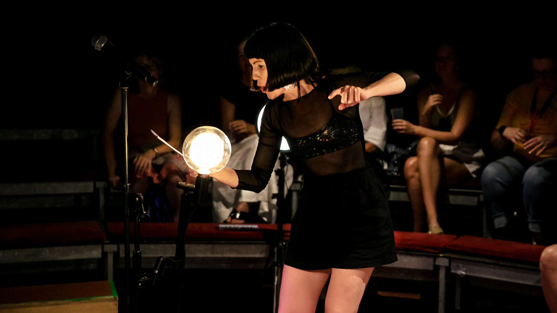 A woman holding a torch as if it were the moon, performing before an audience