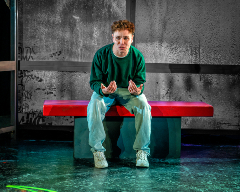 A young man on a bus shelter bench talking to camera