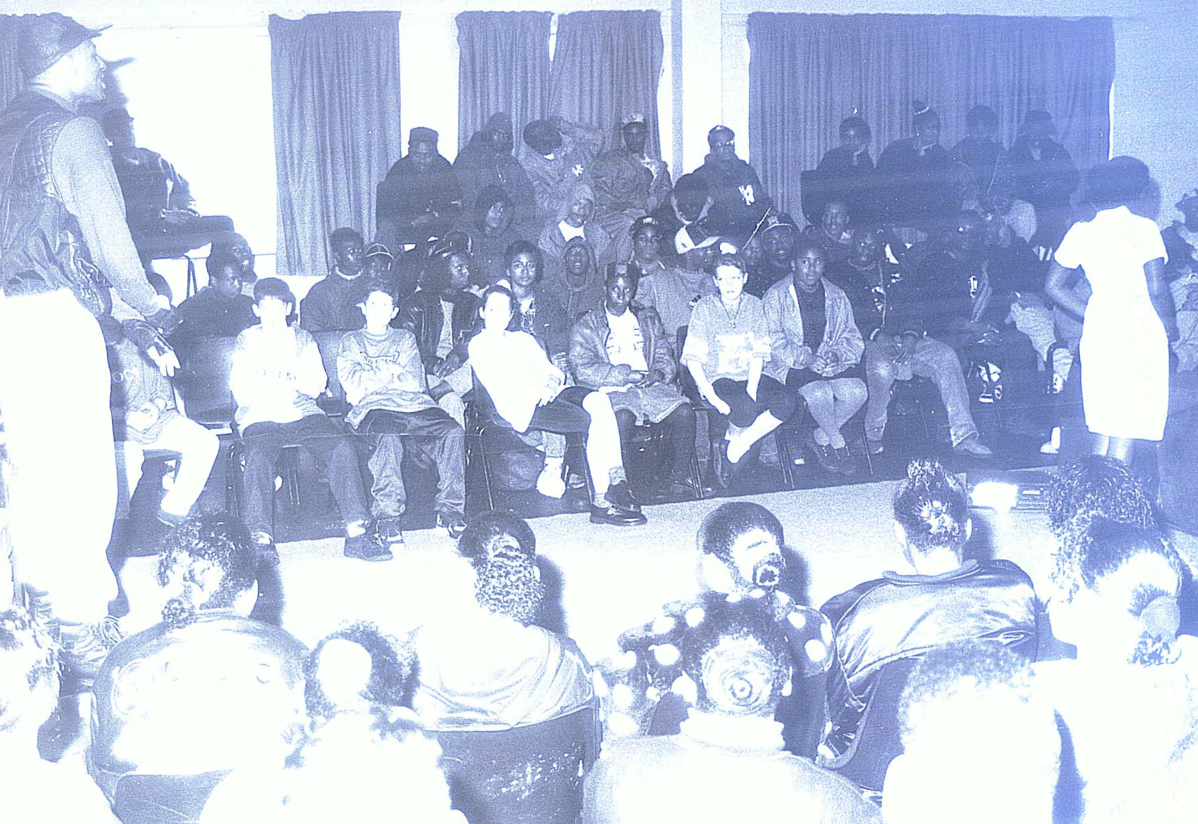 An audience in a large hall sat either side of a stage with a man addressing them
