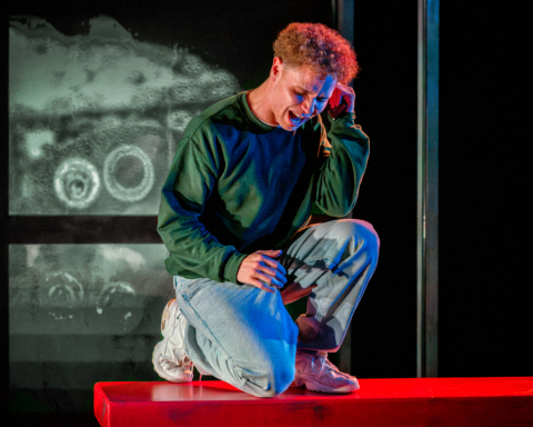 A young man knelt on a bus stop bench holding his head and scrunching his face as if screaming