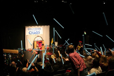 An audience throwing foam javelins at two gladiators on stage