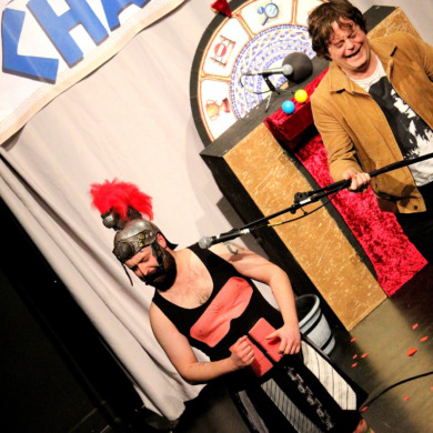 A gladiator with abs stuck on and an audience member holding a weapon